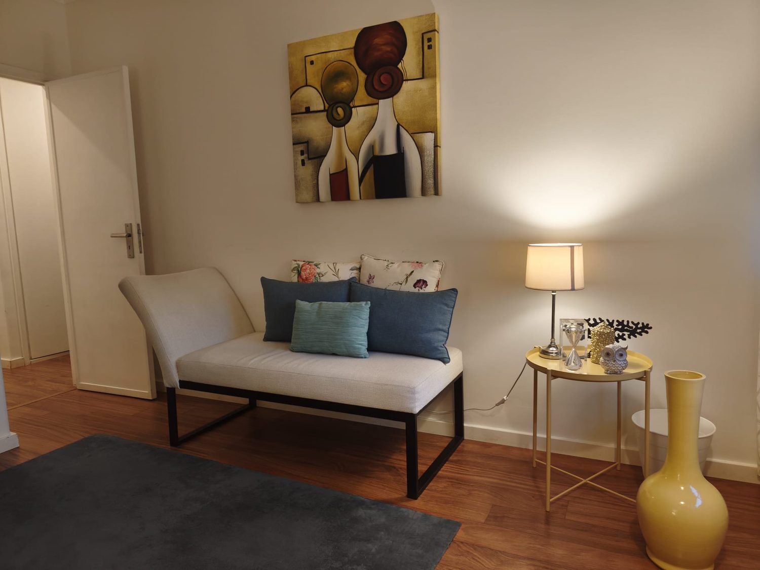 Sofá com almofadas, candeeiro e quadro no consultório